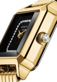 Reloj rectangular color dorado con esfera negra, adornado con cristales y con una correa texturizada. Presenta una corona prominente y acentos claros.