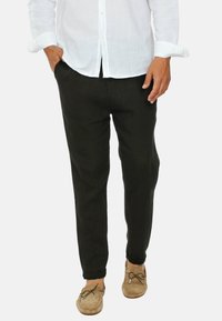 Pantaloni in lino neri con una vestibilità comoda e gamba affusolata. Indossati con una camicia bianca button-up e mocassini color cammello. Texture liscia, design semplice.