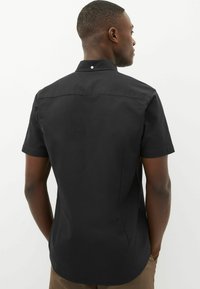 Camisa de manga corta con botones en algodón negro, con canesú en la parte posterior, un solo botón en el cuello y un acabado liso y texturizado.