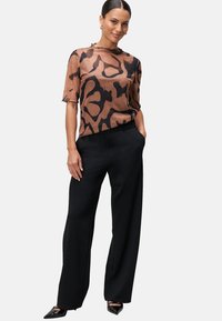 Blouse courte à manches courtes en marron avec des motifs abstraits noirs, associée à un pantalon large noir. Tissu texturé avec des bords ondulés.