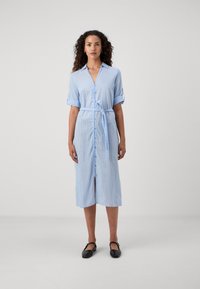 Vestido camisola riscado em azul claro com mangas curtas dobradas, fecho de botões na frente, faixa na cintura e uma fenda na bainha. Material em algodão.