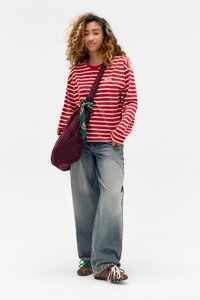 Rot-weißer gestreifter Langarmshirt mit Logo, kombiniert mit hellblauen baggy Jeans. Eine bordeauxfarbene Cord-Crossbody-Tasche mit einem gemusterten Schal.