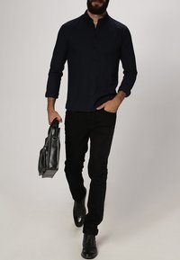 Donkerblauwe overhemdd, zwarte broek en zwarte leren schoenen. Houdt een zwarte leren tas vast. Slim fit, lange mouwen en kraagontwerp.