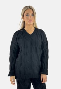 Pull en maille noir avec un décolleté en V, présentant un motif en torsades, des manches amples et un ourlet côtelé. Tissu lisse et texturé.