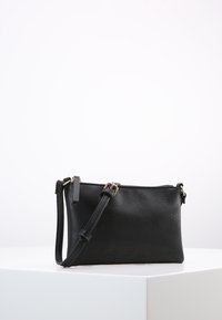 Svart läder crossbody-väska med texturerad yta, guldfärgad hårdvara och ett avtagbart axelband. Kompakt rektangulär form, dragkedjestängning.