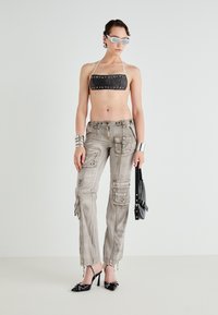 Black studded bikini top, gray cargo pants with multiple pockets, black pointed heels with stud accents, silver bracelets, and sunglasses.