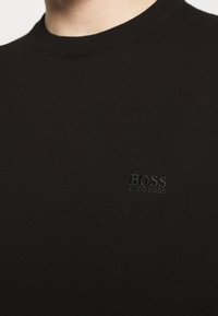 Pull ras du cou en coton noir à maille côtelée avec un logo "BOSS" discrètement embossé sur la poitrine.