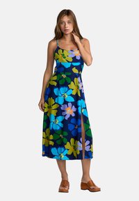 Blumenkleid im Maxiformat mit marineblauem Grundton, das große blaue, grüne und violette Blumen zeigt. Es hat Spaghettiträger und ein seitliches Schlitzdetail.