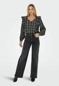 Črna in zelena karirana bluzica z nabranimi rameni, kombinirana z visokimi črnimi kavbojkami in črnimi škornji s peto.