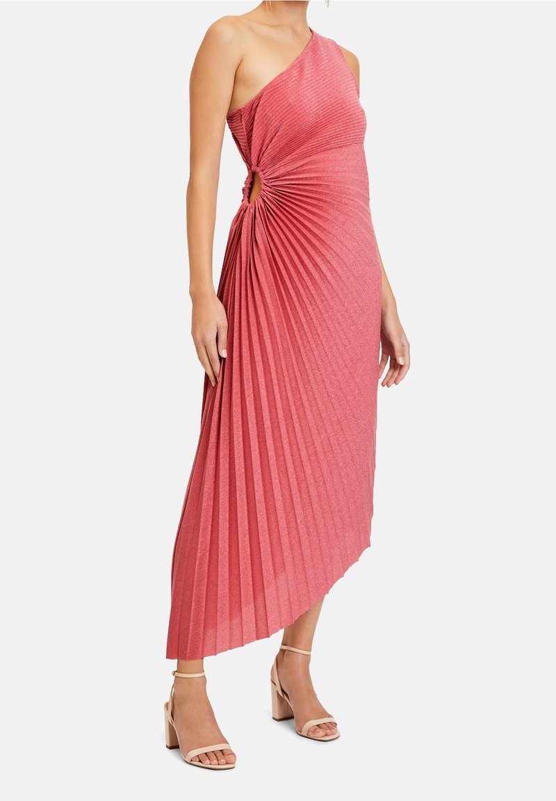 Vestido rosa plisado asimétrico con un nudo lateral y textura metálica, combinado con sandalias de tacón bloque de color claro.
