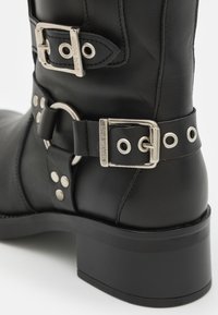 Fekete bőr csizma ezüst csatokkal, szegecsekkel és szellőzőkkel, blokk sarkú kivitelben, a fém alkatrészen "Steve Madden" felirattal.
