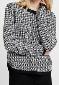 Pullover mit einem schwarz-weißen texturierten Strickmuster, rundem Halsausschnitt und gerippten Bündchen und Saum. Hat eine lockere Passform und ein modernes Design.