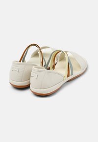 Beige nahka sandaalit avoimella takana, joissa on värikkäitä elastisia hihnoja ruskeana, keltaisena ja sinisenä, sekä joustava kumipohja.