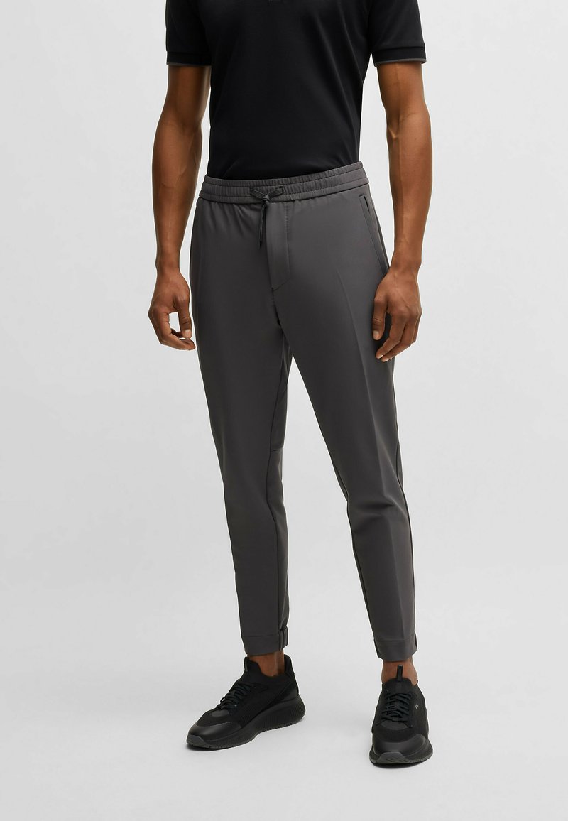 Graue Jogginghose mit schmalem Schnitt, elastischem Bund und Kordelzug. Hergestellt aus leichtem, glattem Material. Mit Reißverschlusstaschen akzentuiert.