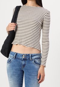 Top de manga larga de canalé crema con rayas horizontales negras; combinado con unos jeans de mezclilla azul claro ligeramente desgastados con cierre de doble botón.