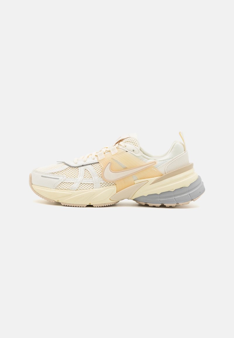 Zapatillas Nike con parte superior de malla y sintético en crema y naranja claro, con una suela gruesa gris y cordones blancos. Presenta elementos de diseño elegantes.