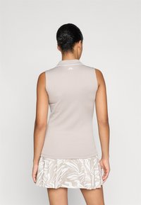 Polo sin mangas en color beige con textura acanalada y ribete blanco; combinada con una falda que presenta un patrón de hojas en tonos claros.