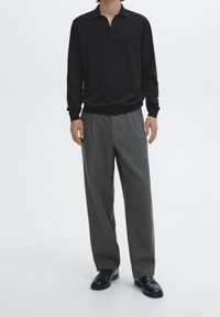 Sort polo med lange ærmer og en halvspalte, kombineret med grå højttaljede, vide bukser og sorte loafers. Minimalistisk design.