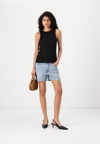 Svart ribbad ärmlös topp med vågiga kanter, tillsammans med ljusblå denimshorts. Håller en brun handväska och bär svarta slingback-klackar.