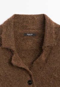 Collo di un cappotto di lana marrone e peloso con bottone nero e etichetta Massimo Dutti cucita all'interno del collo.