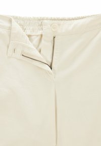 Ljusbeige byxor med elastisk midja, framfickor med dragkedja och knappstängning. Tillverkade av ett slätt och hållbart tyg med rena sömmar.