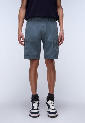 Pantalones cortos cargo en gris pizarra, con bolsillos laterales, cierre de botón y una tela suave y texturizada. Combinados con zapatillas altas.