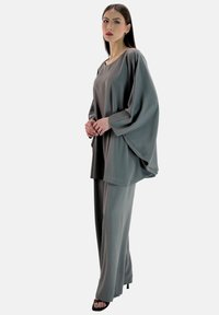 Grau, zweiteiliges Outfit bestehend aus einer locker sitzenden Bluse mit weiten Ärmeln und passenden weit geschnittenen Hosen, gefertigt aus einem glatten, leichten Stoff.