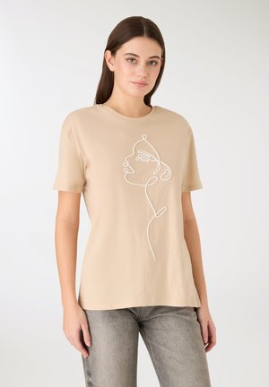 T-shirt beige in cotone con disegno in linea bianca di un volto. Maniche corte, scollo rotondo e vestibilità rilassata. Design semplice e minimalista.