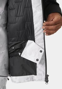 Schwarze und graue isolierte Jacke mit gestepptem Innenfutter. Eine Seitentasche mit Druckknopfverschluss. Reißverschluss vorne mit strukturierten Stoffakzenten.