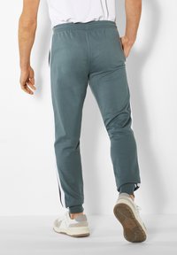 Türkise Fleece-Jogginghosen mit seitlichen Taschen, weißen Streifen entlang der Seiten, schmaler Schnitt und elastischem Bund. Kombiniert mit weißen Sneakers.