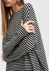 Top a righe bianco e nero a maniche lunghe caratterizzato da una vestibilità comoda, scollatura ampia e maniche oversize con orlo irregolare.