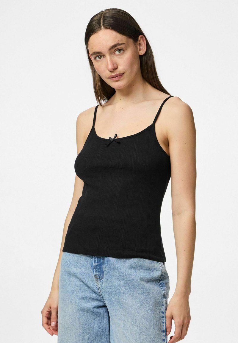 Débardeur noir à côtes avec de fines bretelles spaghetti, présentant un petit accent de nœud noir au niveau du col. Texture lisse et coupe ajustée.