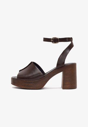 Brown leather platform sandal with open toe, ankle strap with gold buckle, and chunky wooden block heel.