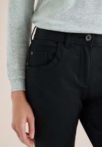 Zwarte broek van textuurstof, rechte pasvorm, met voorzakken en knoopsluiting, gecombineerd met een lichtgroene top met spikkels en lange mouwen.