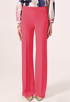 Pantaloni a gamba larga fucsia aderenti, realizzati in un tessuto liscio e elasticizzato, senza chiusure visibili, abbinati a décolleté dorate a punta.
