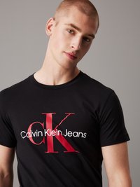Black t-shirt made of cotton with short sleeves, featuring bold red "CK" logo and white text "Calvin Klein Jeans" on the front.