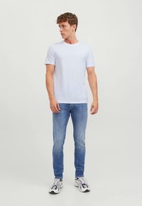 Valge puuvillane T-särk lühikeste varrukatega, kombineeritud helesiniste teksade ja halli-valgete spordijalanõudega. Lihtne disain ja mitteametlik sobivus.