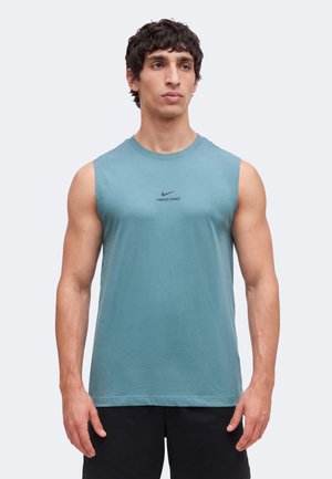 Homme portant un débardeur bleu Nike Pro et un short noir, debout devant un fond clair uni, faisant face à l'avant.