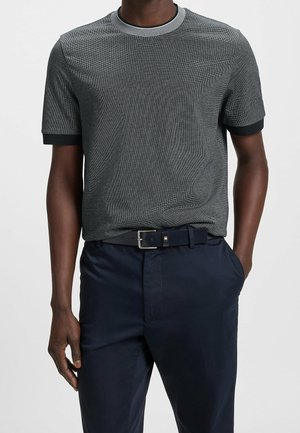 Chemise à manches courtes grise texturée avec des accents noirs et gris clair au col et aux poignets, associée à un pantalon bleu marine et une ceinture noire.