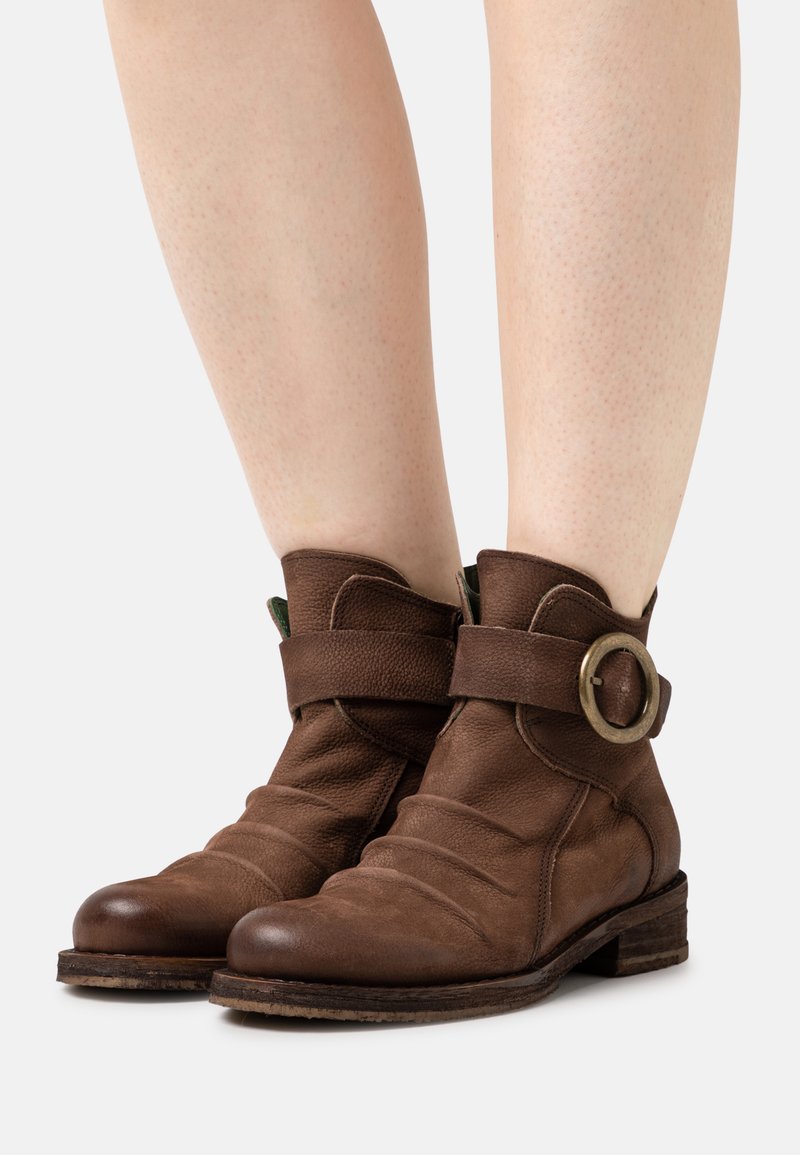 Botins de couro castanho até ao tornozelo com ponta arredondada, design solto, uma faixa larga com uma fivela circular metálica e um salto baixo em camadas.