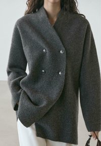 Giacca in misto lana grigia con design doppiopetto, grandi bottoni e maniche larghe, che crea una silhouette rilassata e oversize.