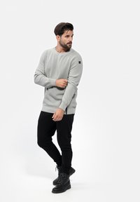 Sweatshirt ribbed gris clair avec des manches longues et un accent noir sur l'épaule, associé à un pantalon noir fuselé et des bottes noires.