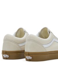 Beige sneakers med overdel i semsket skinn og lerret, hvite skinnaksenter, polstret krage, og gummisåle med "VANS"-logo.