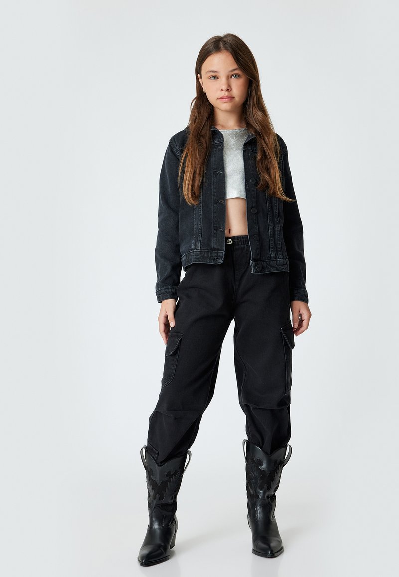 Svart denimjacka, kort. Grå stickad topp under, svarta cargobyxor med fickor. Svarta cowboyboots med dekorativa detaljer.