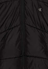 Schwarze Steppjacke mit einem vorderen Reißverschluss, ausgestattet mit einer genähten Textur und einem kleinen gestickten CK-Logo im linken Brustbereich.