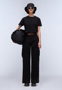 Černé bavlněné tričko, černé cargo kalhoty s kapsami, hnědý opasek, černý klobouk typu bucket, bílé sluneční brýle a černá taška na rameno.