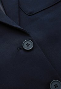 Tissu bleu marine foncé avec deux boutons ronds à quatre trous et une couture de revers pliée sur un vêtement sur mesure.