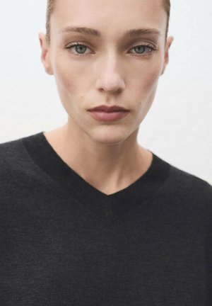 Pull noir en V en tissu doux, présentant un design ajusté et une texture lisse, vue rapprochée de l'encolure et des épaules.