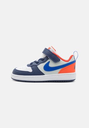 Niedriger Kindersneaker in Weiß, Navy, Blau und Orange mit Klettverschluss, Schnürsenkeln und gepolsterter Sohle auf einem schlichten Hintergrund.