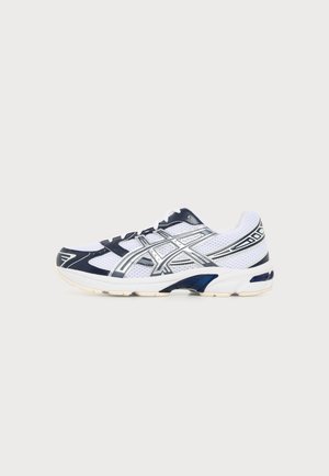 Scarpa da corsa atletica bianca e blu navy con strisce logo argento e lacci bianchi su uno sfondo chiaro uniforme.